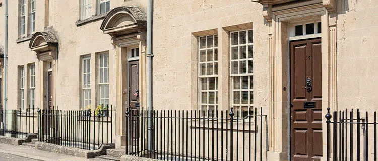 Landscape image of row of houses in Bath City, uniform look with same style throughout, brown doors and black railings.