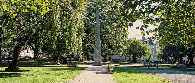 Landscape image of park in Bath city centre with trees and sculpture in centre shot