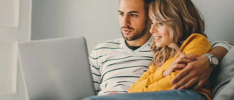 Image of couple sat on sofa looking at a laptop together.