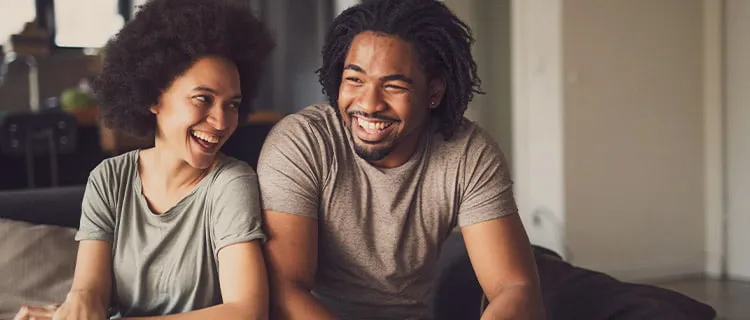 Landscape image of man and woman sat on the sofa talking and laughing.