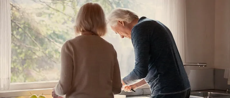 Landscape image of man and woman hunched over a kitchen worktop preparing food.