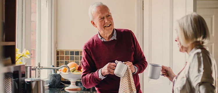 Landscape image of man and woman drying tea cups in the kitchen talking to each other.