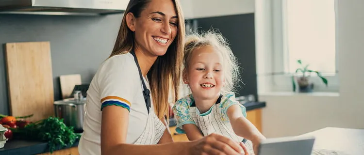 Woman and child both engaging with tablet computer screen and laughing at what's on the screen. Sat at kitchen worktop at home.