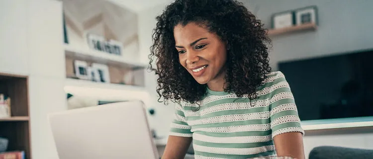 Landscape image of woman sat at laptop screen at home working from home.