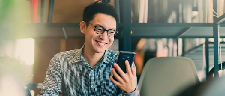 Landscape image of man looking at his mobile phone screen and laughing.