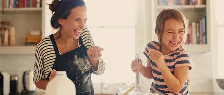 Wide landscape image of mother and daughter making food together in the kitchen mixing with whisk and laughing.