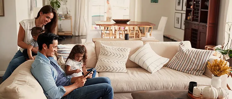 Family sat on corner sofa in home, man using iPad and mother sat on sofa holding baby