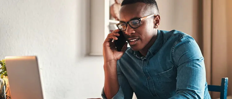 Close up of man sat at laptop on the phone with a mug of coffee on the desk.